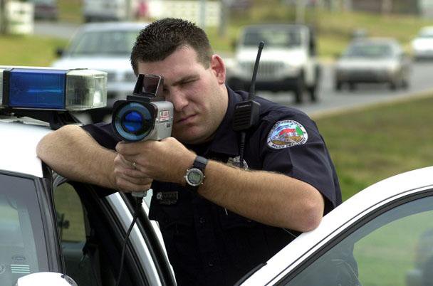Police officer shooting radar gun standing next to police car