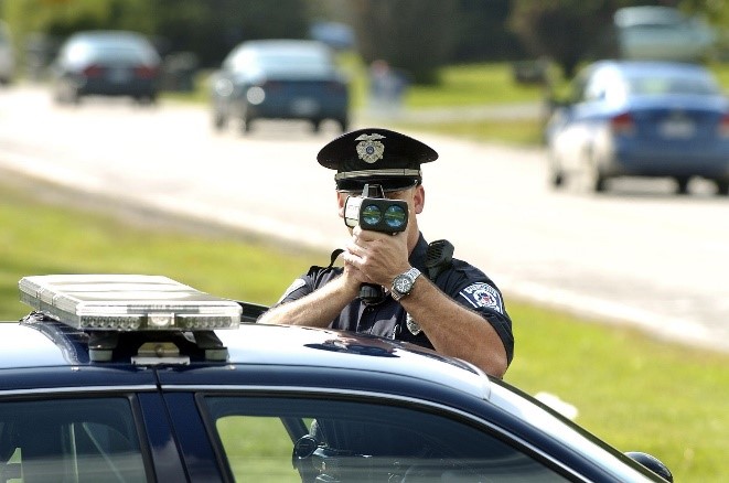 Police officer using laser radar gun with elbows braced on top of police car
